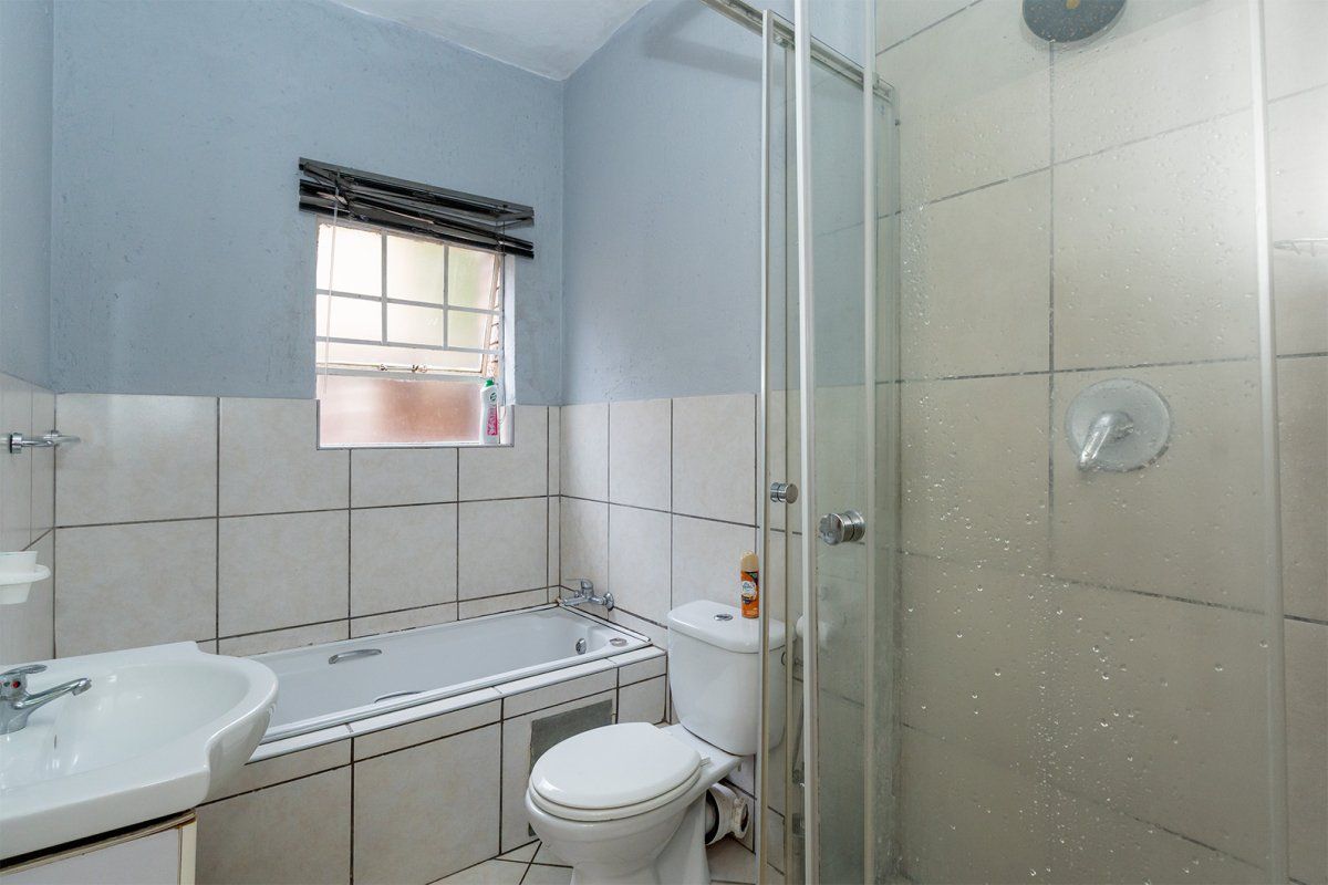 A functional bathroom featuring a combined bathtub and shower enclosure, pedestal basin, and toilet with neutral wall and floor tiling.