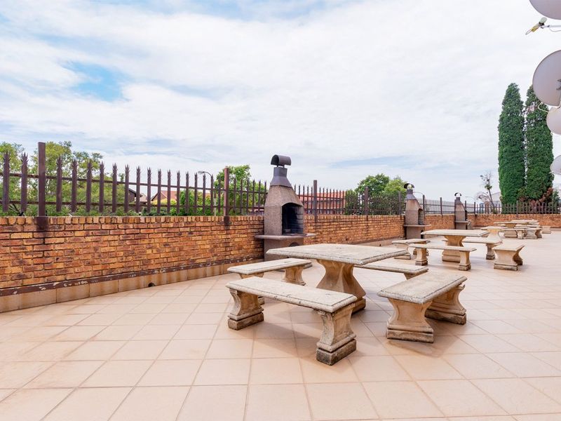 Spacious outdoor patio area featuring tiled flooring, built-in masonry braais, and a brick boundary wall with security fencing.