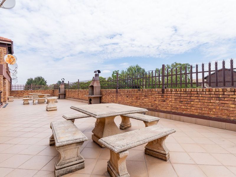 Spacious outdoor patio area featuring built-in brick braai facilities, tiled flooring, and secure perimeter walling, ideal for communal outdoor entertaining.