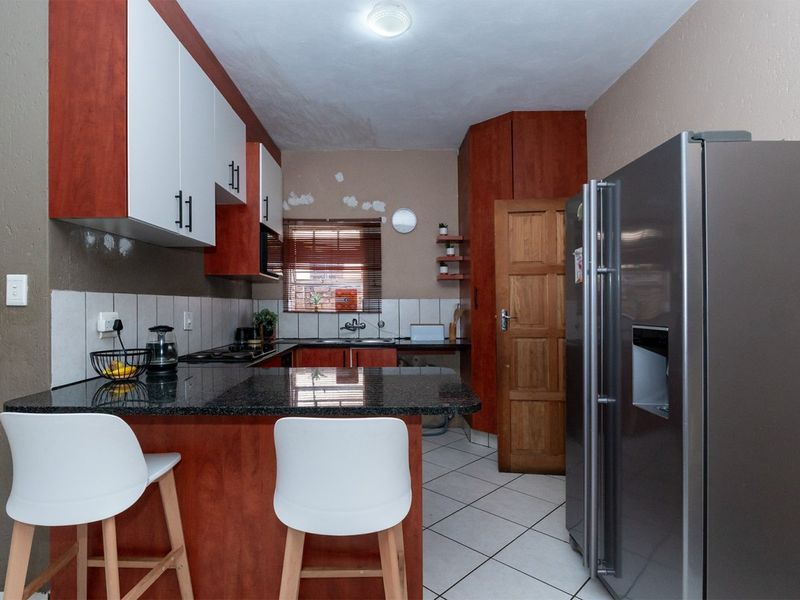 A compact kitchen featuring granite countertops, two-tone cabinetry, and tiled flooring, requiring minor cosmetic repairs to the wall finishes.