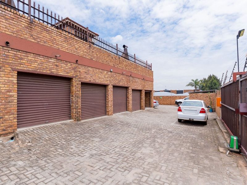 Exterior view of a multi-unit garage block featuring brick construction, roller shutter doors, and a paved driveway with secure perimeter fencing.