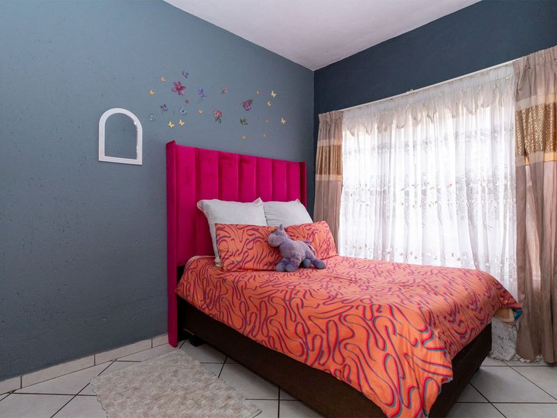 A bedroom featuring tiled flooring and a large window with installed curtain rails, finished with a dark blue accent wall.