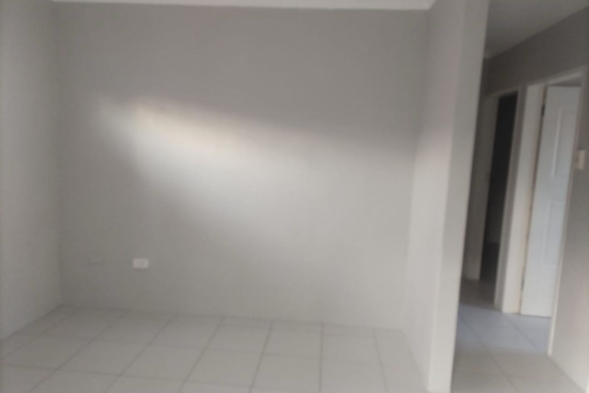 An empty living area featuring neutral wall paint, tiled flooring, and simple cove cornicing, providing a blank canvas for interior design.