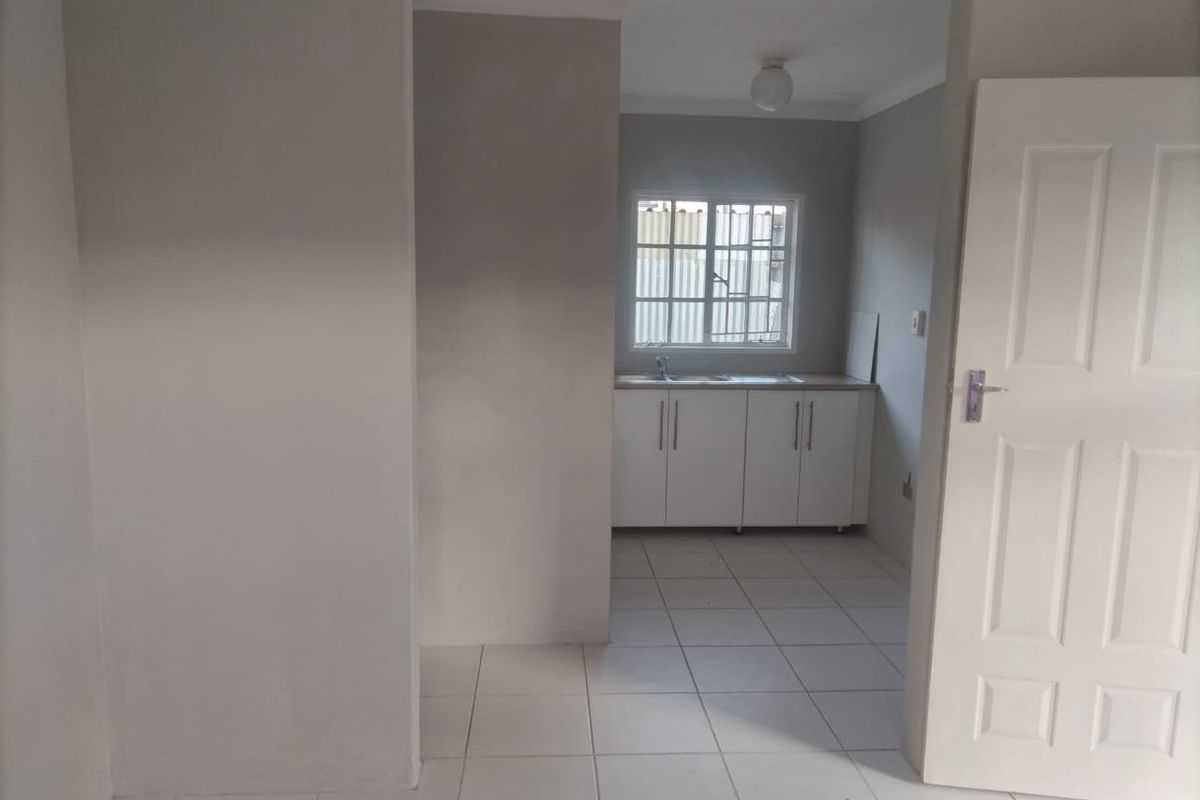 A simple, functional kitchen area featuring white cabinetry, a stainless steel sink, and tiled flooring, presented as a clean, empty space.