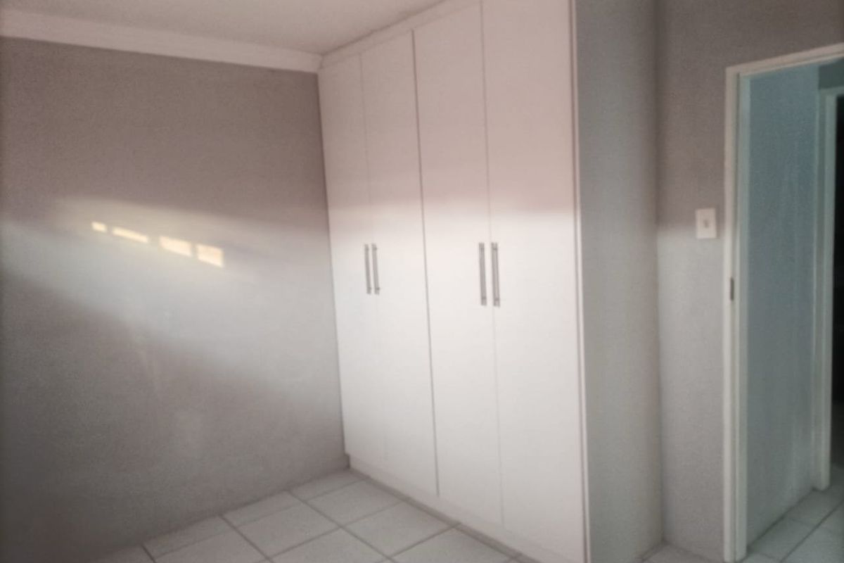 A clean, empty bedroom featuring neutral grey walls, white built-in cupboards, and tiled flooring, offering a blank canvas for personalization.