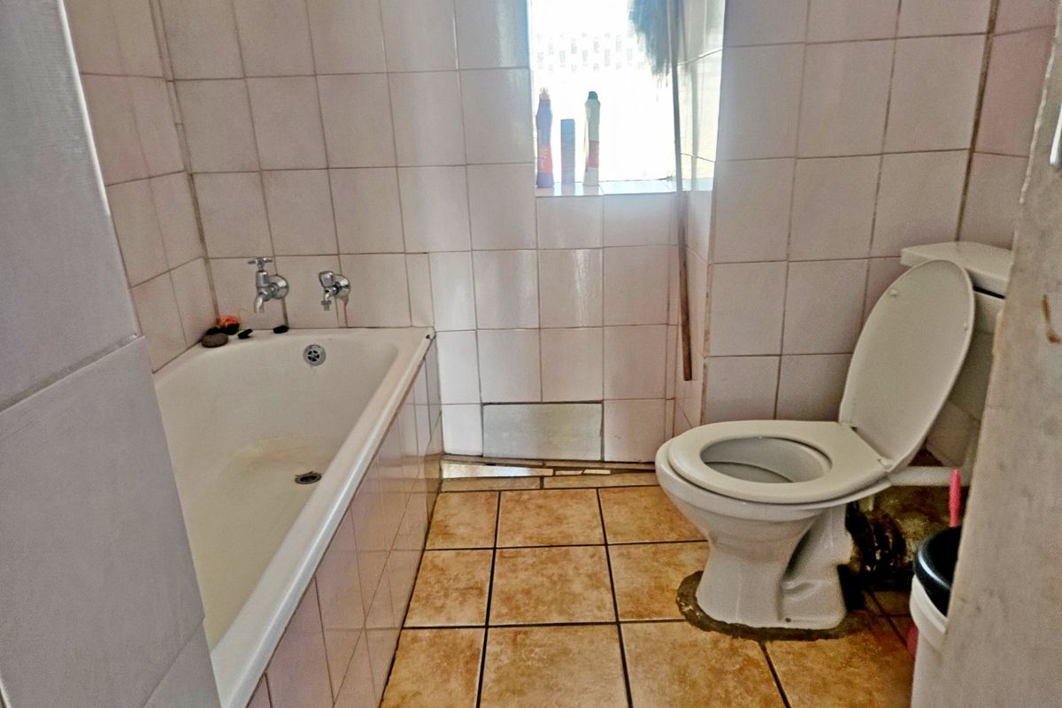 A dated bathroom featuring a standard bathtub, toilet, and ceramic tiling throughout. The space requires cosmetic updates and repairs to the flooring.