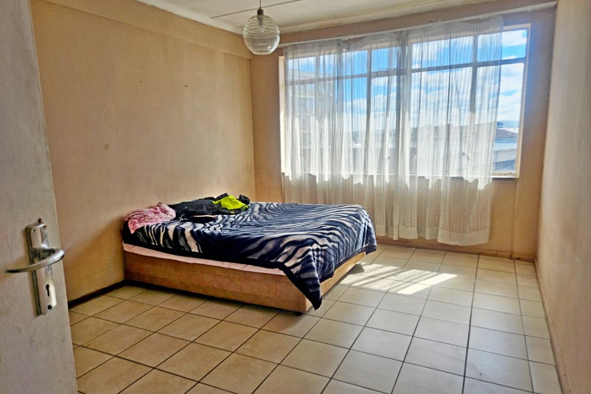 A bedroom featuring tiled flooring and a large window providing natural light. The space requires cosmetic updates to the walls and ceiling.