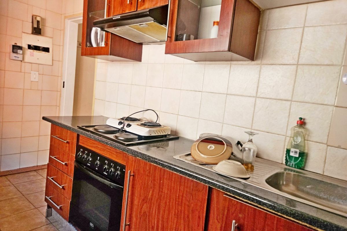 A functional kitchen featuring wood-look cabinetry, a built-in oven with extractor fan, and tiled splashbacks, offering a practical layout for daily meal preparation.