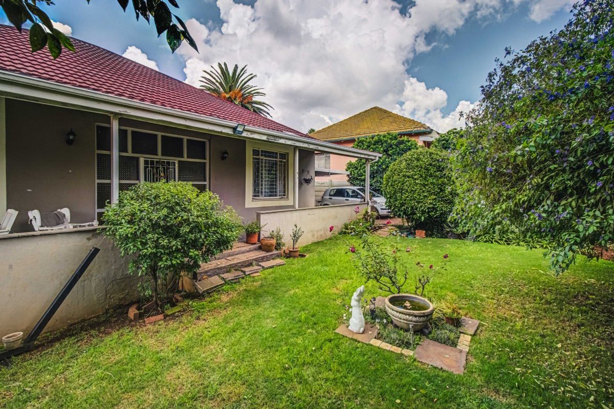 A view of the rear exterior of the house featuring a covered patio, tiled roof, and a well-maintained garden area.