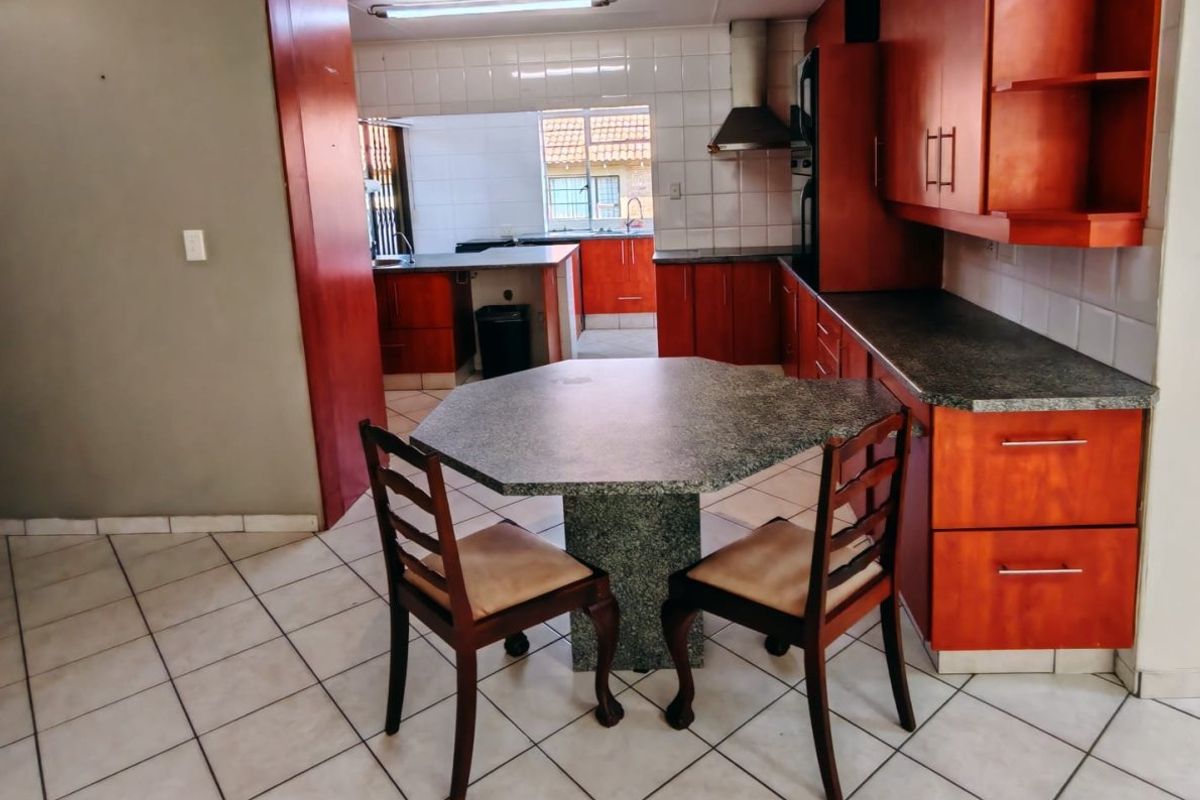A functional kitchen featuring wood-tone cabinetry, granite-look laminate countertops, tiled flooring, and a built-in oven with an extractor fan.