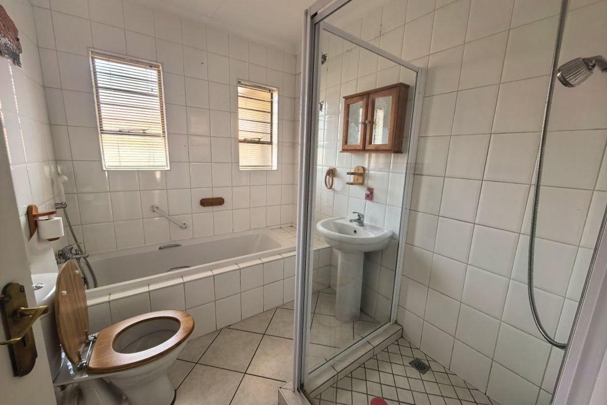 A functional bathroom featuring a built-in bathtub, separate shower enclosure, pedestal basin, and full-height wall tiling.