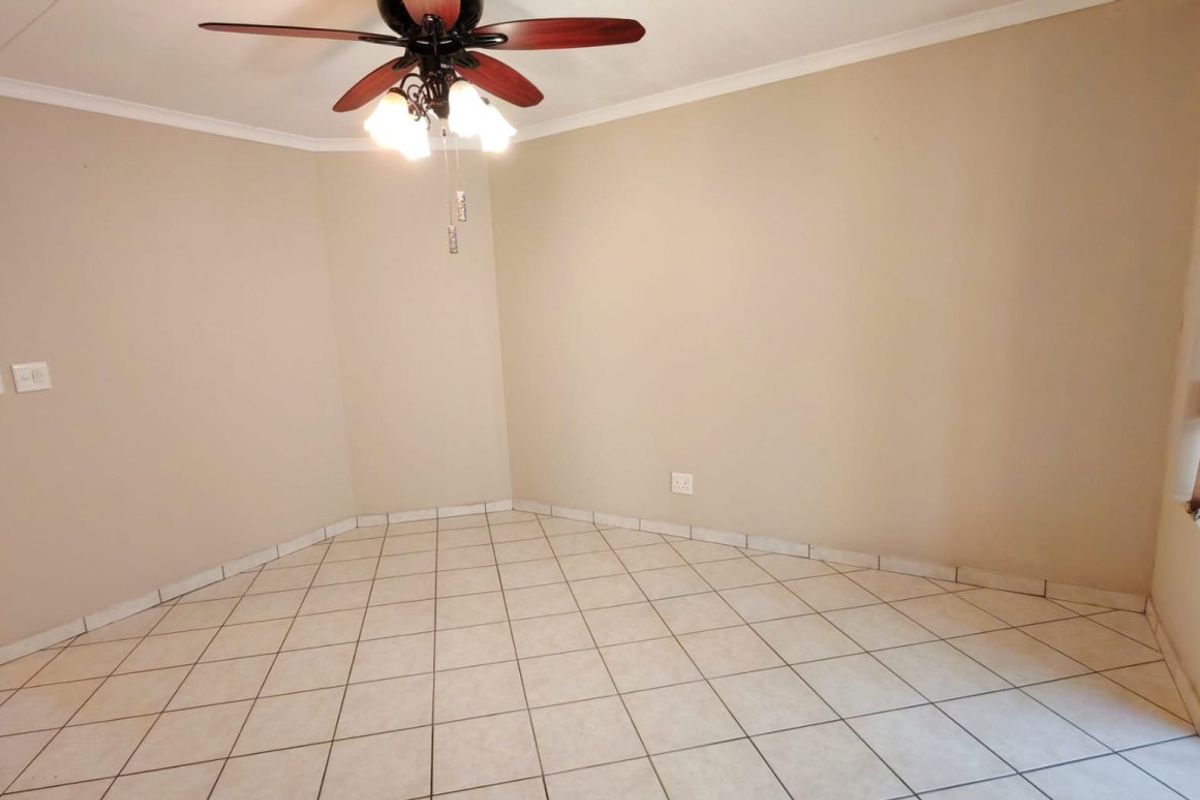 An empty living area featuring neutral wall paint, ceramic floor tiles, and a ceiling fan with integrated lighting.