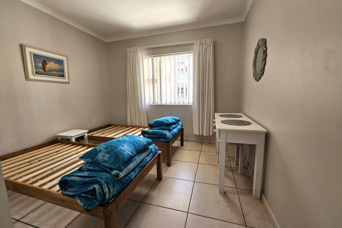 A functional bedroom featuring tiled flooring, neutral wall finishes, and a window with vertical blinds, providing a clean and simple living space.