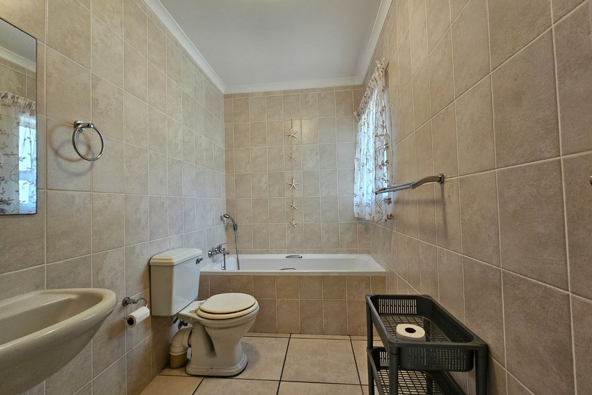 A functional bathroom featuring a built-in bathtub, wall-mounted basin, and toilet, finished with neutral ceramic wall and floor tiles.