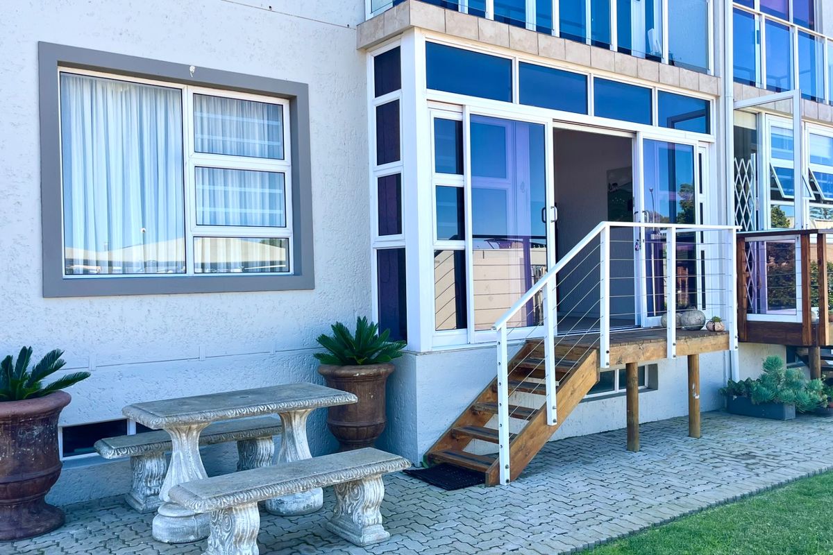 Rear exterior view of the apartment featuring a paved patio area, timber staircase with metal balustrade, and sliding glass doors leading to the interior.