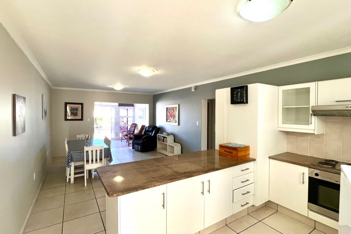 Open-plan living area featuring a functional kitchen with granite countertops, built-in oven, and hob, flowing into a dining space and adjacent living area.