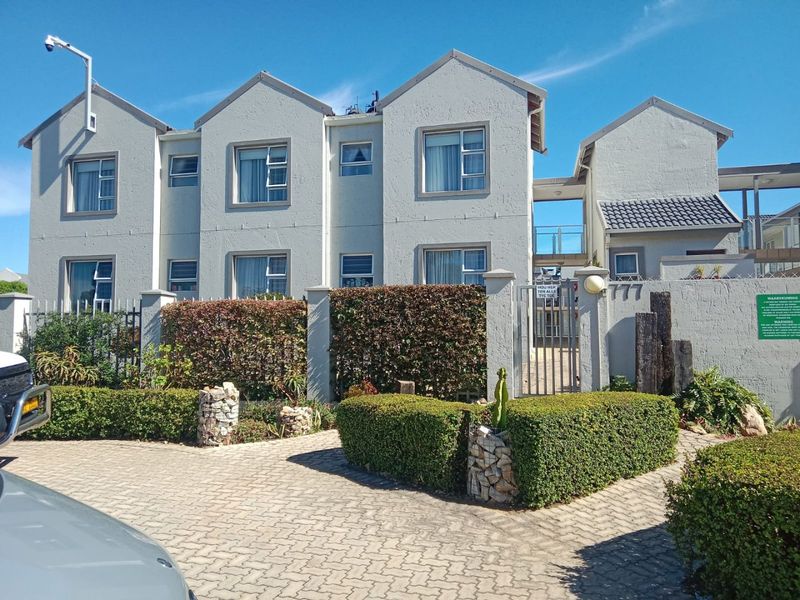 Front elevation of a multi-story apartment complex featuring a paved driveway, secure gated entrance, and well-maintained landscaped hedging.