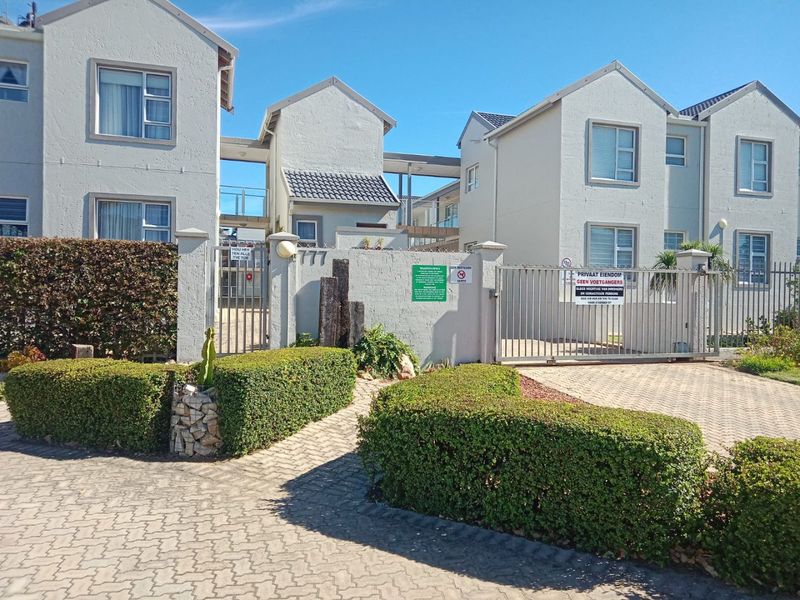 Front exterior view of a residential apartment complex featuring a secure gated entrance, paved driveway, and well-maintained perimeter landscaping.
