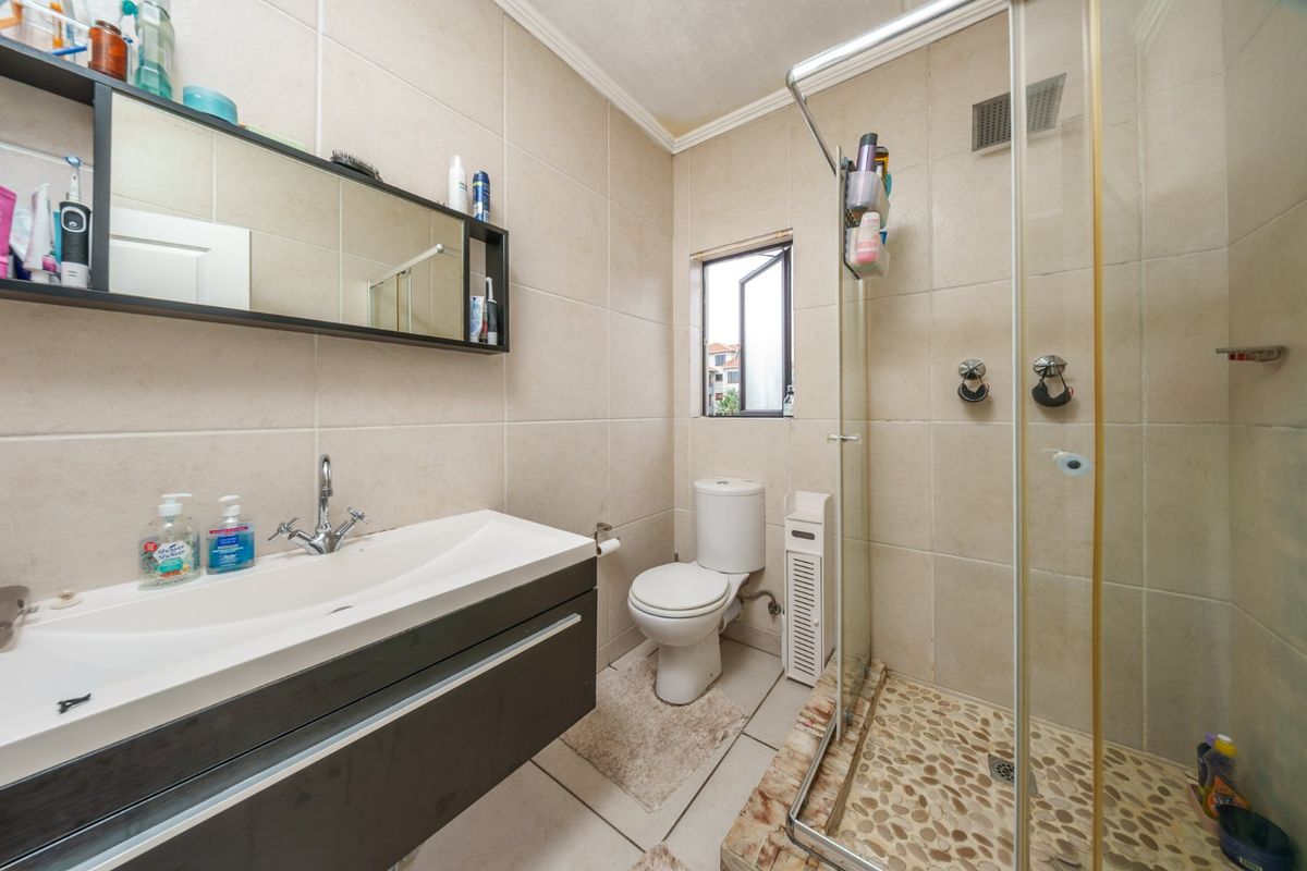 A functional bathroom featuring a vanity cabinet, toilet, and a walk-in shower with a pebble floor finish and neutral wall tiling.