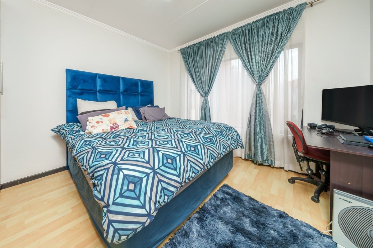 A well-maintained bedroom featuring light-toned laminate flooring and large windows dressed with curtains.