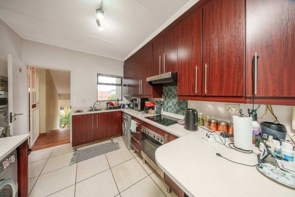 A functional kitchen featuring dark wood-finish cabinetry, light countertops, tiled flooring, and integrated appliances including an electric hob and oven.