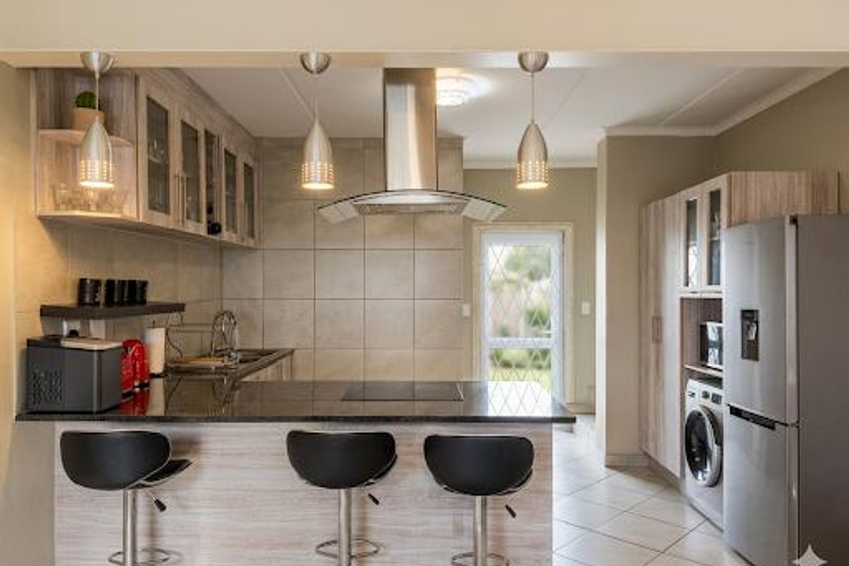Modern kitchen featuring granite countertops, stainless steel extractor fan, ample built-in cabinetry, and tiled flooring, offering a functional and contemporary cooking space.