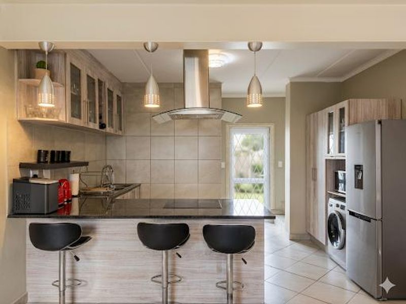 Modern kitchen featuring granite countertops, stainless steel extractor fan, ample built-in cabinetry, and tiled flooring, offering a functional and contemporary cooking space.