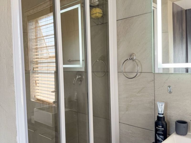 Modern bathroom featuring a glass shower enclosure, vanity with granite countertop, vessel sink, and an illuminated LED mirror.