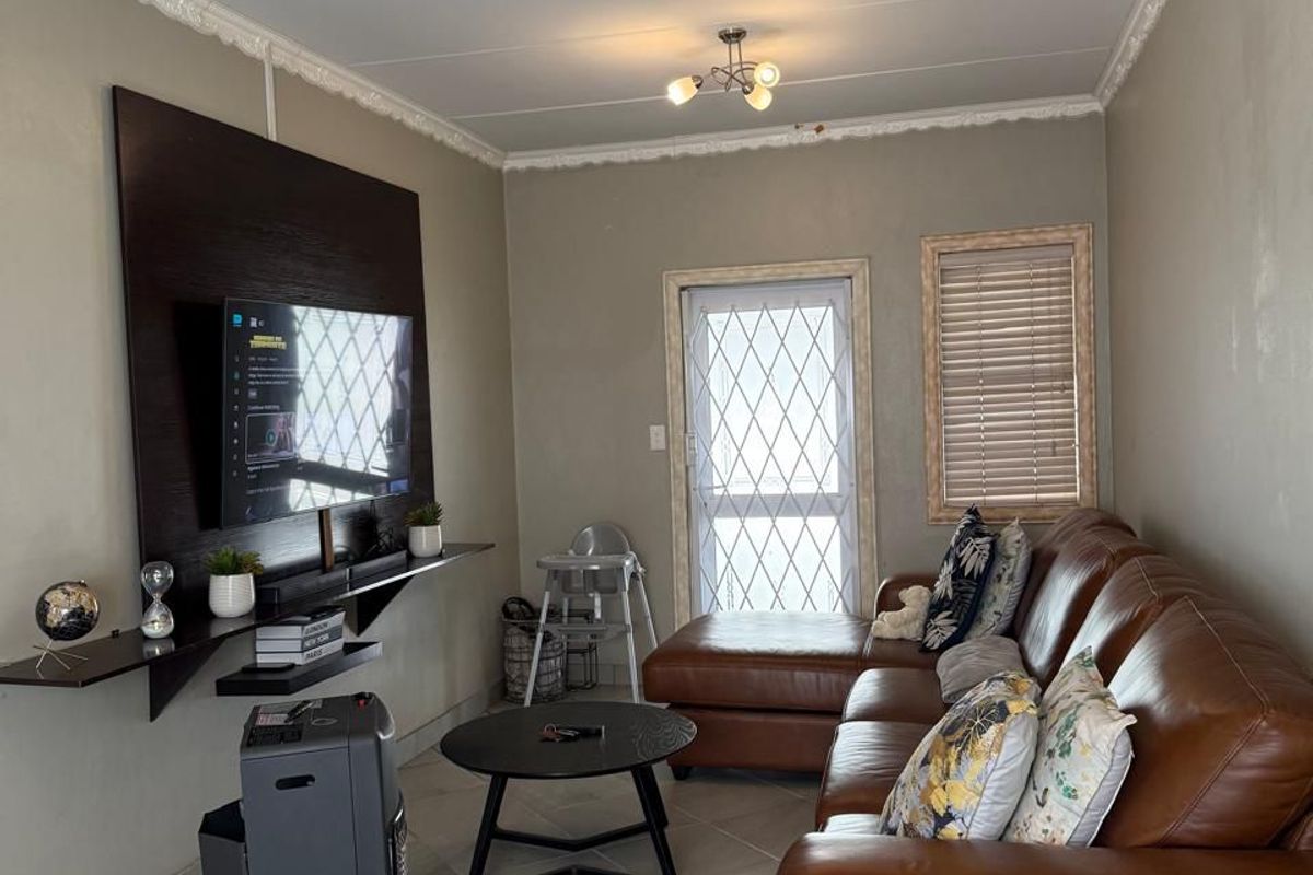 A living room featuring tiled flooring, decorative ceiling cornices, and a wall-mounted media shelf, with access to an exterior security gate.