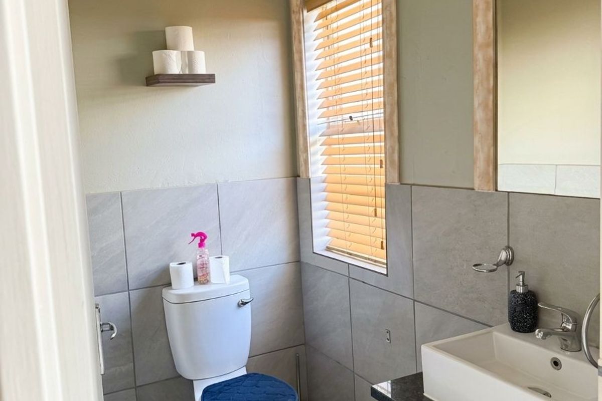 A compact bathroom featuring a modern vanity with a basin, tiled walls, and a toilet, complemented by natural light through venetian blinds.