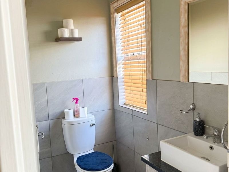 A compact bathroom featuring a modern vanity with a basin, tiled walls, and a toilet, complemented by natural light through venetian blinds.