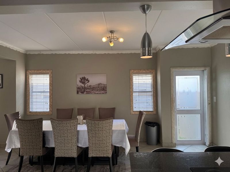A well-lit dining area featuring decorative cornicing, pendant lighting, tiled flooring, and a frosted glass exterior door providing natural light.