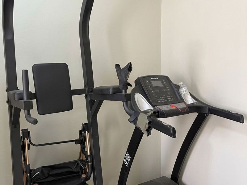 A corner space currently utilized as a home gym area with neutral wall finishes and tiled flooring.