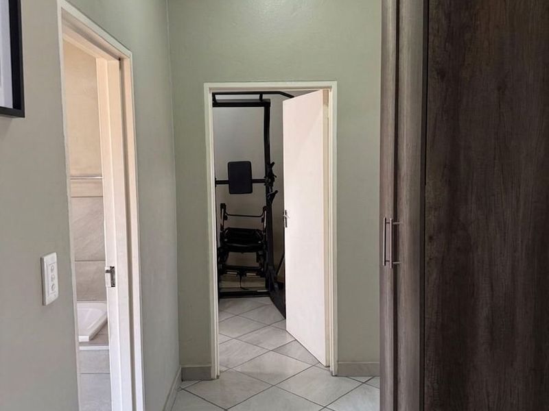 A clean hallway featuring tiled flooring, neutral wall paint, and a built-in cupboard, providing access to adjacent rooms.