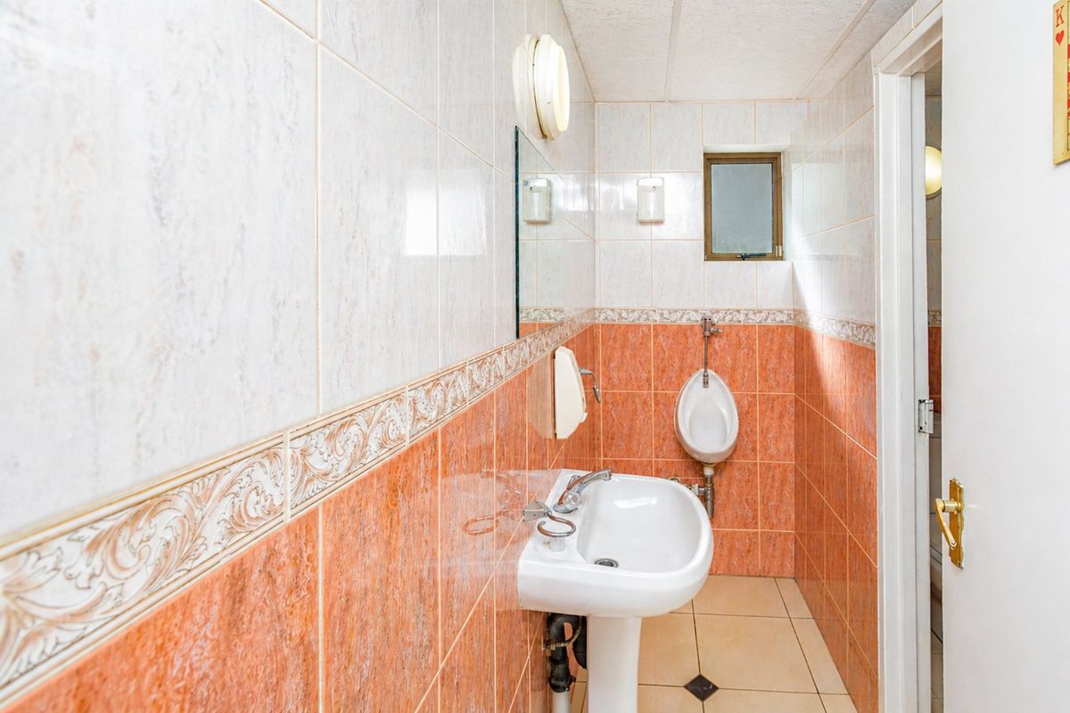 A functional commercial bathroom featuring a pedestal sink, wall-mounted urinal, and two-tone ceramic wall tiling.