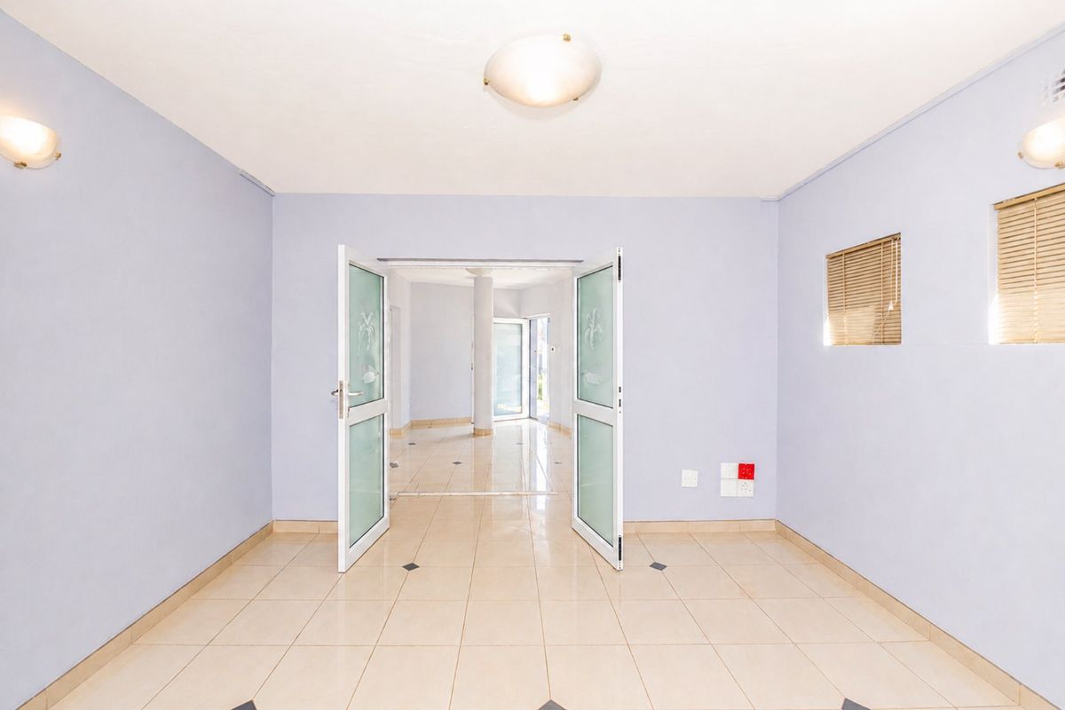 An empty, light-filled living area featuring tiled flooring, double glass doors leading to an adjacent space, and neutral wall finishes.