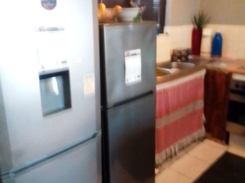 A compact kitchen area featuring tiled flooring, a stainless steel sink, and a window with blinds, currently showing dated finishes.