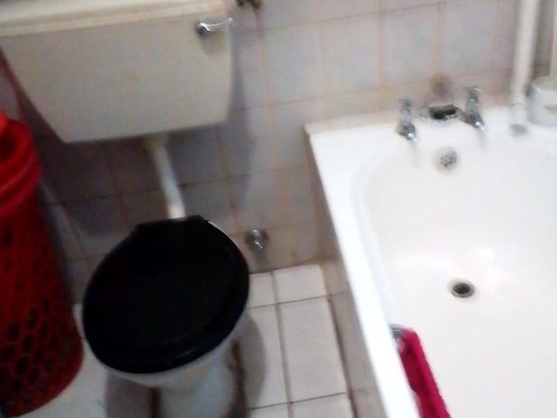 A functional bathroom featuring a standard bathtub and toilet with tiled finishes, currently showing signs of wear and requiring maintenance.