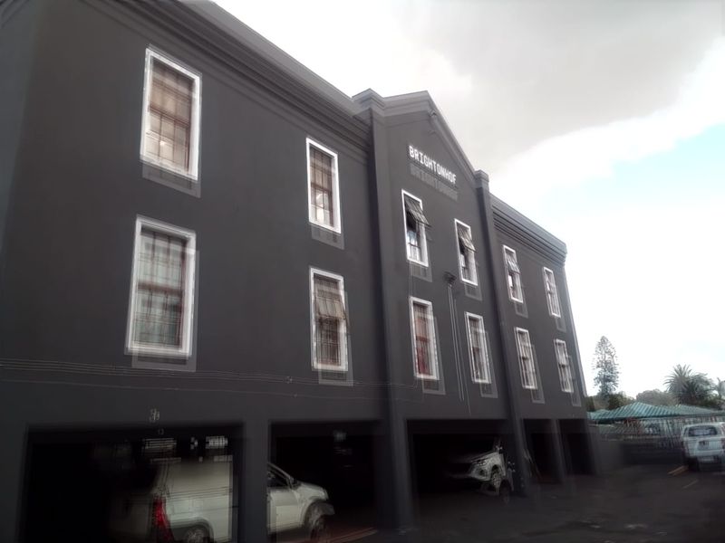Exterior view of the Brightonhof apartment building featuring a dark facade, multi-level sash windows, and ground-level covered parking bays.