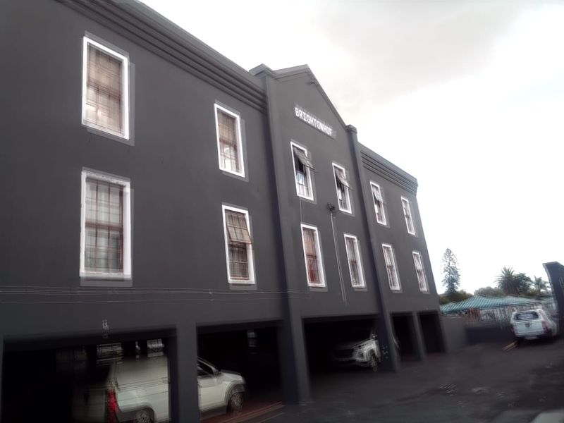 Exterior view of the Brightonhof apartment building featuring a dark facade, sash windows, and ground-level covered parking bays.