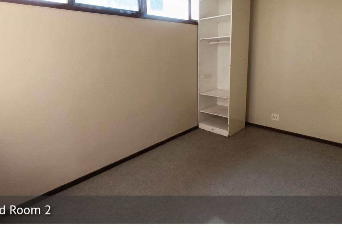 A vacant bedroom featuring neutral wall finishes, carpet flooring, and a built-in shelving unit.