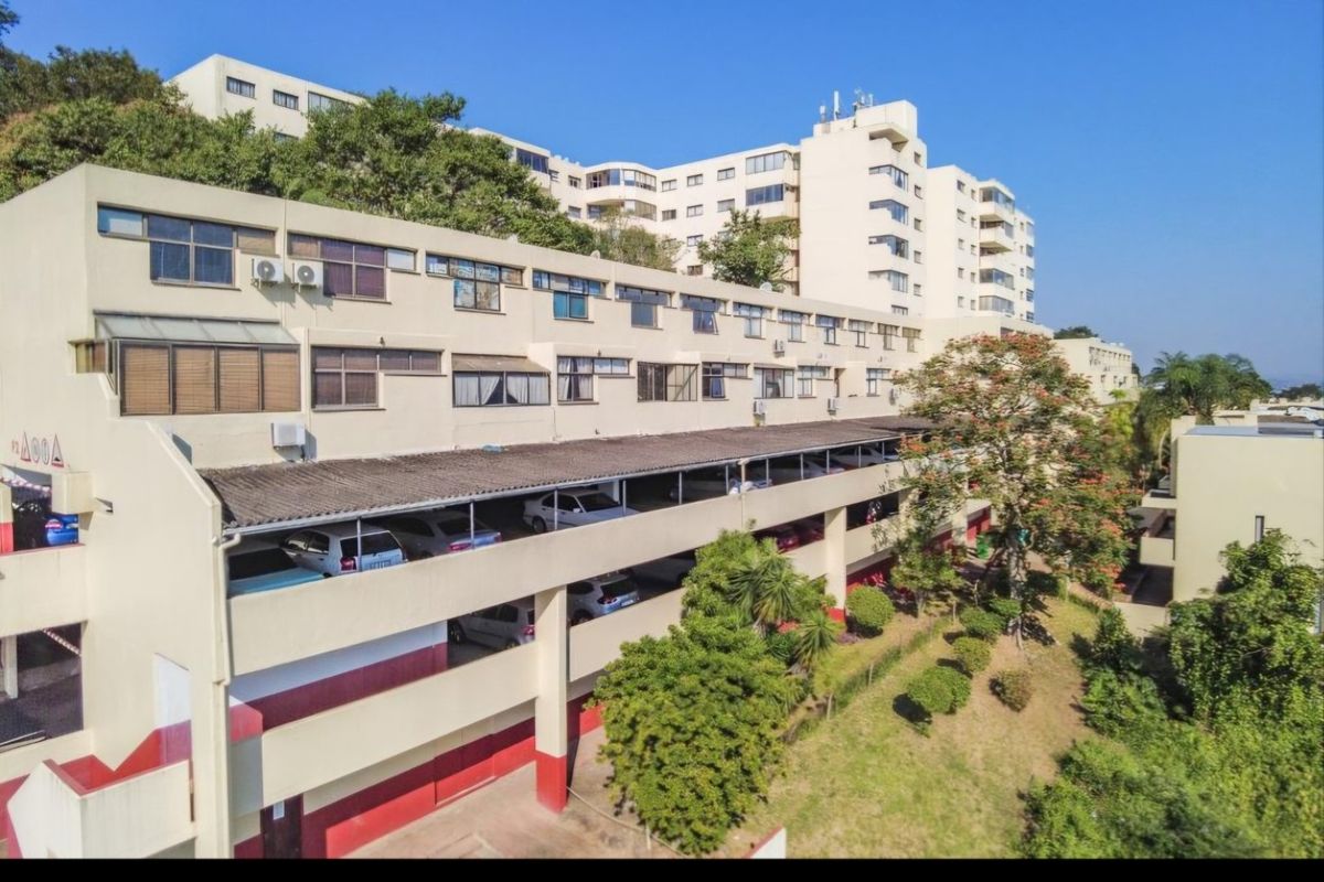 An elevated view of the apartment complex rear facade, featuring a multi-level covered parking structure and established landscaped grounds.