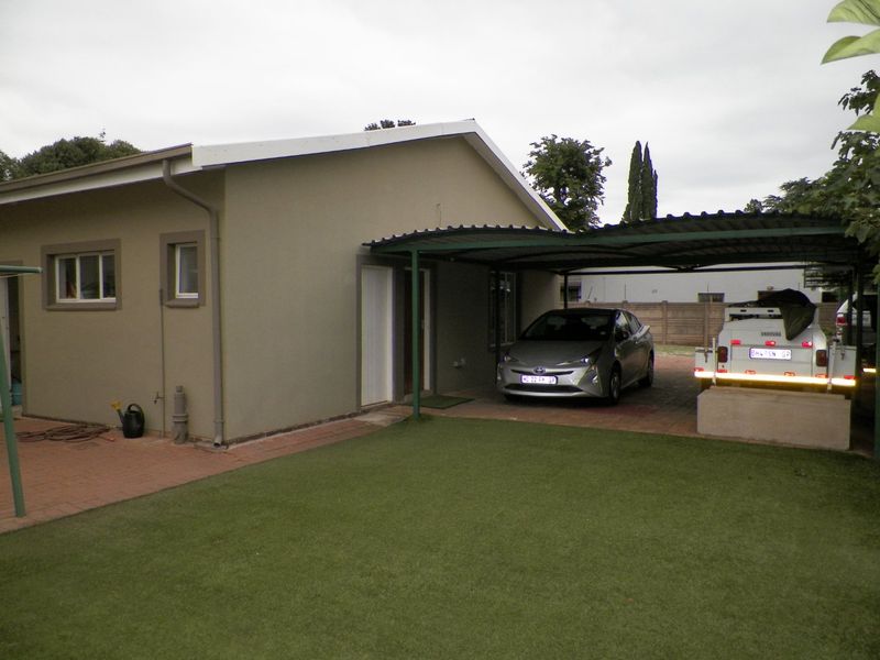 Rear exterior view of the property featuring a covered carport, paved driveway area, and low-maintenance artificial lawn.