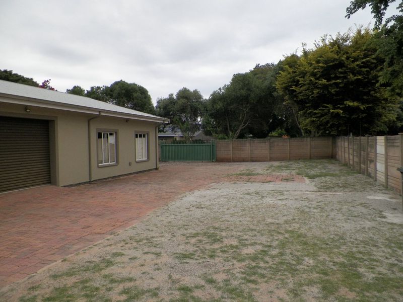 Rear exterior area featuring a brick paved driveway, roller garage door, and enclosed by precast concrete boundary walls with a metal gate.