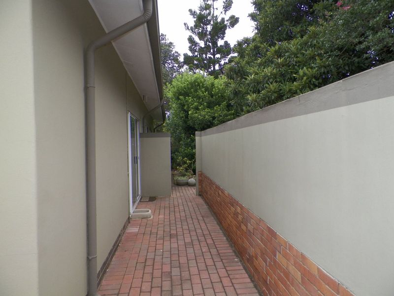 A side walkway featuring brick paving, a solid boundary wall, and access to the home via a sliding glass door.