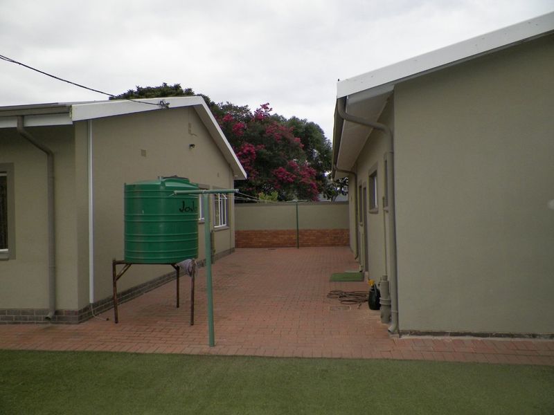 Rear exterior area featuring brick paving between two building structures, including a water tank and perimeter boundary wall.