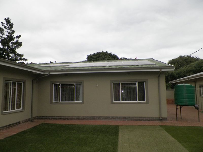 Rear view of the house featuring a corrugated metal roof with installed solar panels, aluminium windows, and an elevated water storage tank.