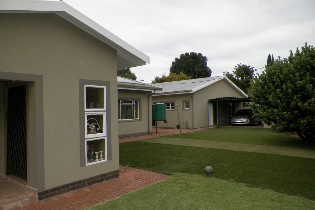 Rear view of the property featuring a well-maintained lawn, brick paved pathways, a water tank, and a covered carport area.
