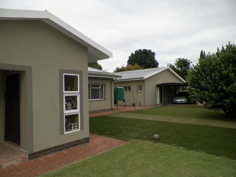 Rear view of the property featuring a well-maintained lawn, brick paved pathways, a water tank, and a covered carport area.