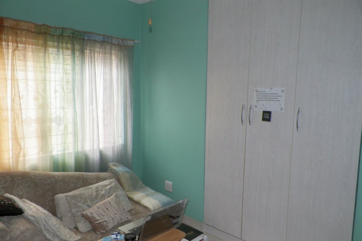 A bedroom featuring a built-in wardrobe, light green walls, and a window with security bars.